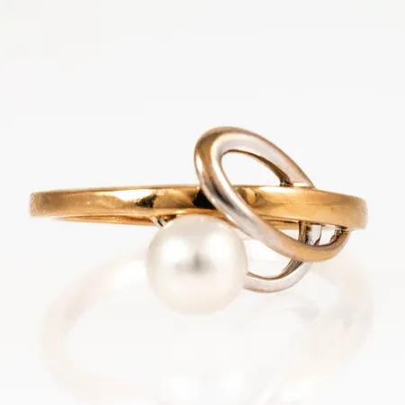 Ring i 18K guld med en odlad vit pärla Ø 6,5 mm. Den är i storlek 18½, är 2 - 12 mm bred och väger 4,8g. Något bortnött rhodiumyta på dekor.