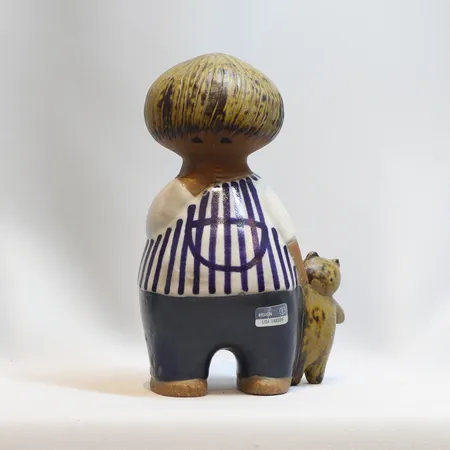 Figurin Malin, Lisa Larson, ur serien Larsons ungar, Gustavsberg, i produktion 1962-1980, höjd ca 18cm, delvis glaserad samt bemålad stengodslera, signerad LL, etikettmärkt Skickas med postpaket.