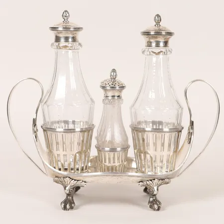 Bordssurtout i sengustaviansk stil, fasetterade glasflaskor samt ströare med lock, ställ 27x11cm & flaskor 19,5x6,8cm respektive 13x3,8cm, Anders Fredrik Weise (1776-1808), Stockholm år 1795, defekt dekor på hals av ströare, åldersbetingat slitage, silver. Vikt: 1464 g