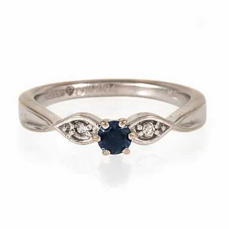 Ring i 14K vitguld med safir och 2 x ca 0,015ct briljantslipade diamanter. Den är i storlek 17½, är 2 - 4 mm bred och väger 3,4g. Gravyr. 