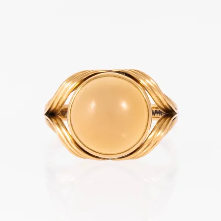 Ring i 18K guld med cabochonslipad sten Ø 11 mm (troligen persikomånsten). Den är i storlek 16½, är 2,3 - 12,5 mm bred och väger 3,4g. Sliten sten. Spricka i skena. 