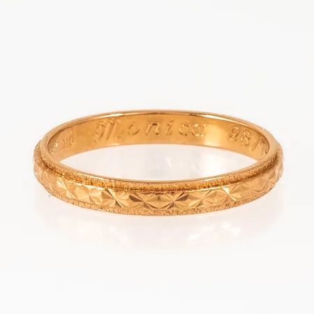 Ring i 18K guld med mönsterdekor. Den är i storlek 18½, är 3 mm bred och väger 2,8g. Stämplad Q10 (1990), BÖS (Bror Schalins Guld, Östersund), 18K & kattfot. Gravyr.