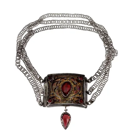 Halslås, silver, röda glasfluss, filigran, mått 44 (50) x 39 mm, tillverkad av Johan Liljedahl Sölvesborg 1810, omändrad till brosch med senare monterad nål och fäste, förstärkt fäste i nederkant, korta kedjor, längd omkring 31 cm, äldre ägargravyr på baksidan 1855 (delvis förstörd p.g.a. monterad förstärkning), smärre bristningar/bruksmärken, stenar med åldersrelaterat slitage Vikt: 50 g