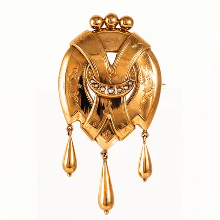 Brosch i 18K guld med småpärlor. Den är 60 x 31 mm och väger 7,5g. Tillverkad 1943 av J Petterssons Eftr Juvelerar AB i Stockholm.