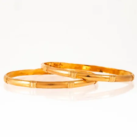 Två armringar i 21K guld. De är 5 mm breda, har en innerdiameter på 65 mm och väger 22,7g. Ojämnheter på insidorna.