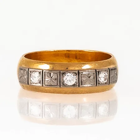 Ring i 23K guld med diamanter 3 x c:a 0,05ct; fattade i vitt guld 18K. Den är 6,7 mm bred, är i storlek 17¾ och väger 8,8g. Gravyr.