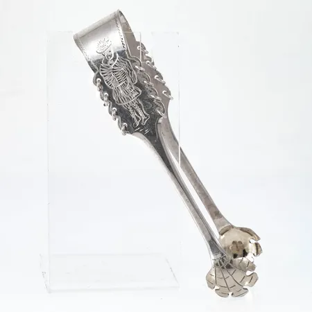 Sockertång i silver (830/1000) med ett handgraverat, samiskt mönster.  Tillverkad 1953 av CO Persson i Haparanda. Den är 10 cm lång och väger 20,0g. Bruksskick.