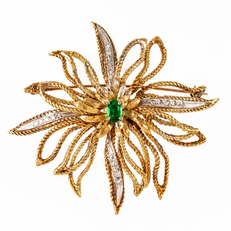 Brosch i 18K guld med en smaragd (6 x 4 mm) & tjugo åttkantslipade diamanter á c:a 0,01ct; fattade i vitt guld.  Den är Ø c:a 59 mm och väger 27,2g bto inkl. metallnål. Stämplad 18K. 