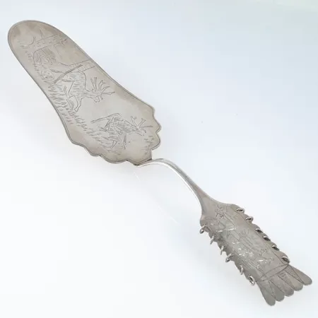 Tårtspade i silver (830/1000) med ett handgraverat samemotiv. Den är 24 cm lång och väger 68,2g. Tillverkad 1934 av CO Persson i Haparanda. Bruksskick. Monogramgravyr.