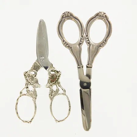 Två druvsaxar, 10,6cm samt 12,3cm, blad i stål, skaft i silver, silver 830/1000 Vikt: 58,1 g