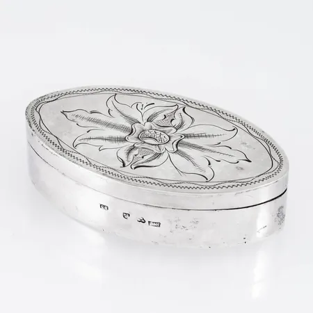 Lockask i silver med fint handgraverat mönster på locket. Den är 72 mm bred, 41 mm djup, 18,5 mm hög och väger 35,4g. Tillverkad 1858 av Erik Erson Linderoth, Umeå. Stämplad med Umeås gamla stadsstämpel.