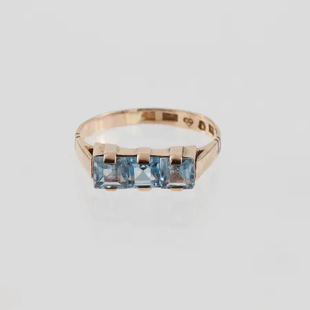 Ring med syntetiska ljusblå stenar , Ge-Kå-Smyckek G Kaplan Stockholm 1949, stl 16½mm, något ojämn form, 18k Vikt: 2,3 g