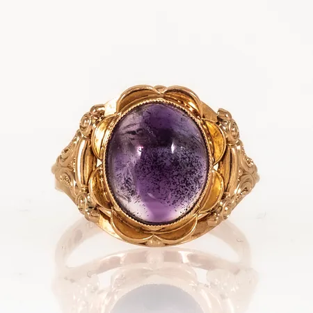Ring i 18K guld med mönsterdekor och en cabochonslipad ametist c:a 11,5 x 9,5 mm. Den är i storlek 17½, är 2,5 - 15,5 mm bred och väger 4,9g. Tillverkad 1954 av G. Dahlgren & Co AB, Malmö). Stämplad 18K & kattfot. Gravyr initialer.