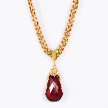 Collier i 18K guld: Dubbelradig cordellänk, integrerat hänge med röd sten. Det är 43 cm långt, 5,4 mm brett och väger 14,4g. Hängets mått 13,8 x 30 mm. Karbinhake. Kedja ihålig. Svaga veck och ojämnheter. 