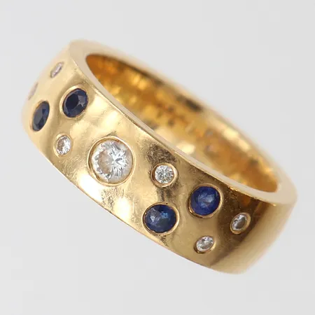 Ring med safirer 4 x ca 0,05ct samt briljantslipade diamanter 1 x ca 0,15ct, 6 x ca 0,02ct, stl: 18, bredd 7mm, 18K.  Vikt: 15 g