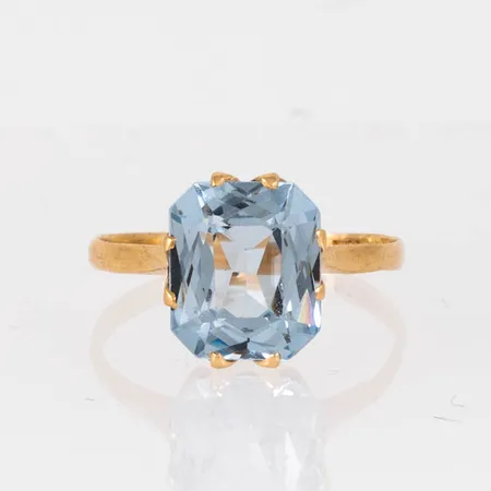 Ring i 18K guld med syntetisk blå spinell 9,5 x 8 mm. Den är i storlek 16½, är 1,6 - 10,5 mm bred och väger 2,1g. Några nagg på fasetterna men väldigt fin lyster på stenen ändå.