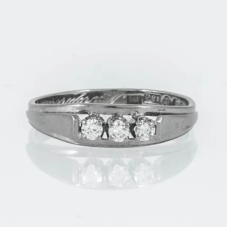Ring i 18K vitguld med 3 x 0,05ct briljantslipade diamanter. Den är i storlek 17½, är 2,5 - 5 mm bred och väger 2,5g. Stämplad M9 (1962), GVH (Guldvaruhuset Aktiebolag, Stockholm), 18K & kattfot. Gravyr.