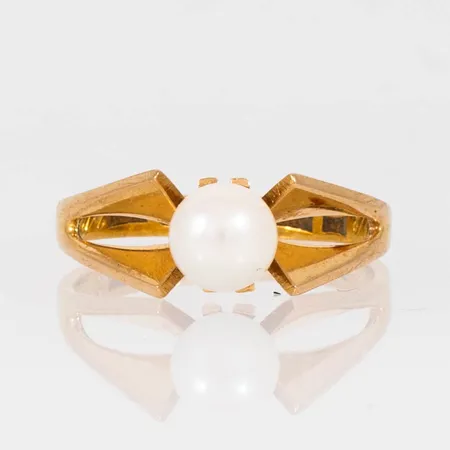 Ring i 18K och 23K guld med vit odlad pärla Ø 6 mm. Den är i storlek 16½, är 2,4 - 7 mm bred och väger 3,5g. Pålödd halvskena i 23K. Gravyr.