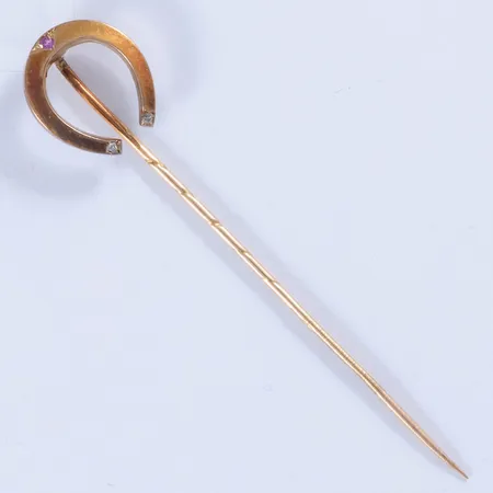 Kravattnål i 18K guld: I form av hästsko med en rosa safir och 2 x c:a Ø 1 mm rosenslipade diamanter. Den är 12 mm bred, 59,5 mm lång och väger 1,2g. Missfärgning. 
