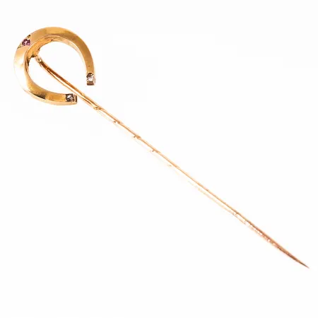 Kravattnål i 18K guld i form av hästsko med en rosa safir och 2 x c:a Ø 1 mm rosenslipade diamanter. Den är 12 mm bred, 59,5 mm lång och väger 1,2g. Stämplad 765. 