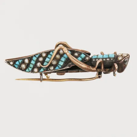 Brosch i form av en gräshoppa med turkoser samt små orientaliska äkta saltvattenpärlor, längd 48cm, ca år 1900, del av låsmekanism av, spröt saknas, två turkoser saknas, silver samt 14K guld, nål i 18K guld. Ask från J.L. Friberg, Stockholm. Vikt: 12,6 g