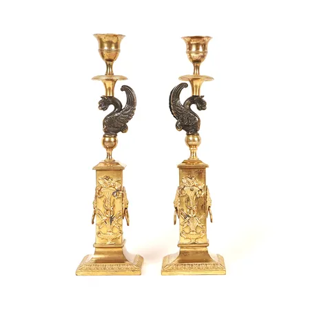 Ett par ljusstakar, senempire, 1800-talets första hälft, brons, stomme med mörkpatinerade gripar och klockformade pipor, postament med lejonmaskaroner och fruktkorgar samt vid foten en bladbård, höjd 26cm, bruks och åldersbetingat slitage, dekordelar något lösa, pipor med mindre skador.