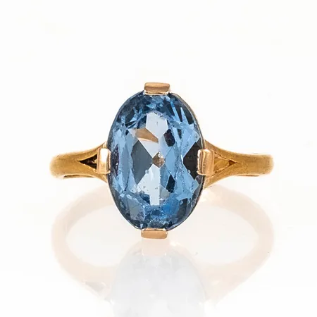 Ring i 23K guld med ljusblå sten i 18K fattning. Den är i storlek 16¾, är 2 - 13 mm bred och väger 3,7g. Gravyr, naggade fasetter.