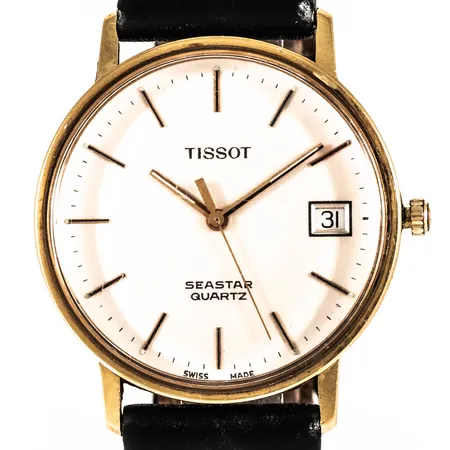 Herrur Tissot Seastar i 18K guld med svart läderband, boett Ø 33,5 mm, datum, quartz, repigt plastglas, gravyr, defekt band. Bruttovikt: 31,4g. Går ej, batteribyte krävs?