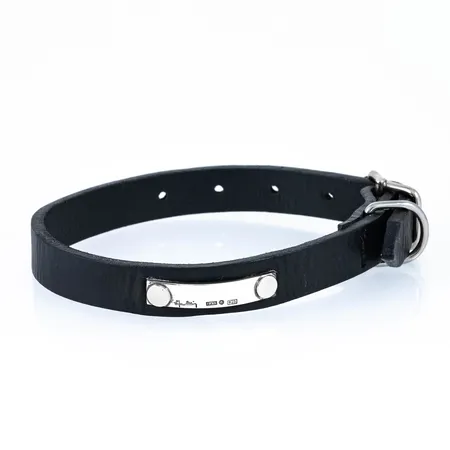 Efva Attling: hundhalsband i svart läder med namnbricka i silver. Brickan signaturstämplad Efva Attling, EFVA, Stockholms stadsstämpel, 925. Det är 16 mm brett. Längd stängt 23 - 31 cm (= till en liten hund). Totallängd 35 cm. Fint skick. 