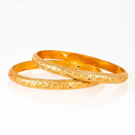 Två armringar i 22K guld. De är 6,3 mm breda, har ett innermått på 17 cm (pyttesmå) och väger 16,7g. Ihåliga ojämnheter.