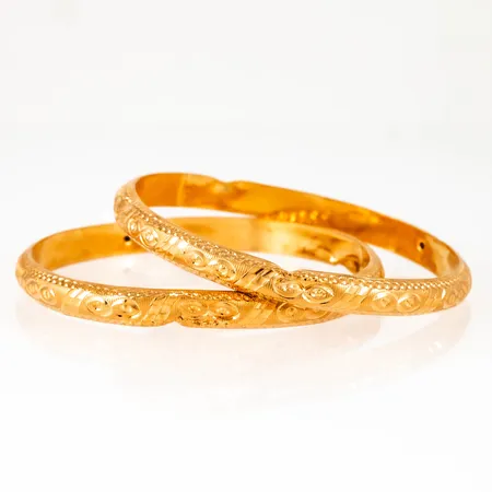 Två armringar i 22K guld. De är 6,3 mm breda, har ett innermått på 17 cm (pyttesmå) och väger 17,0g. Ihåliga ojämnheter. Rejäla klämskador.