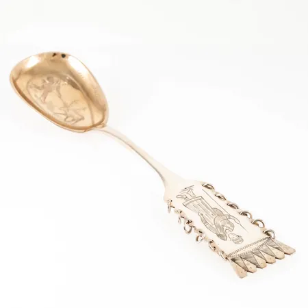 Uppläggningssked i silver med handgraverat samemotiv. Delvis förgylld (nött). Den är 210 mm lång och väger 50,0g. Från CO Persson i Haparanda. Bruksskick.