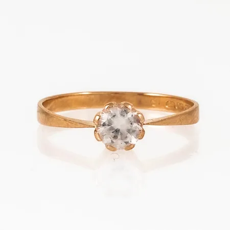 Ring i 18K guld med en vit sten. Den är i storlek 17, är 2 - 5,5 mm bred och väger 1,5g. Naggade fasetter.