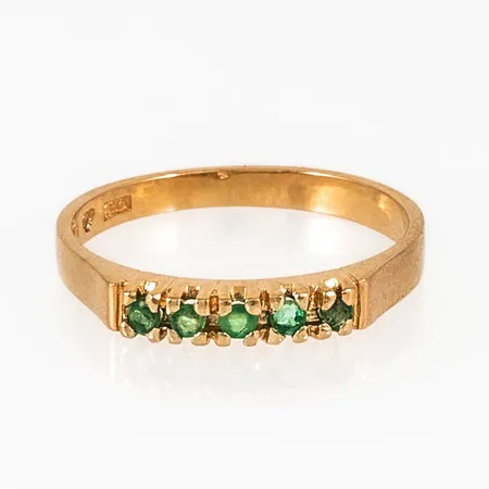 Ring i 18K guld med fem smaragder Ø c:a 1,7 mm. Den är i storlek 16¾, är mm bred och väger 2,2g. Stämplad X10 (1996), BEH (Bengt Hallberg Guldsmeds AB, Köping), 18K & kattfot. En skadad sten.