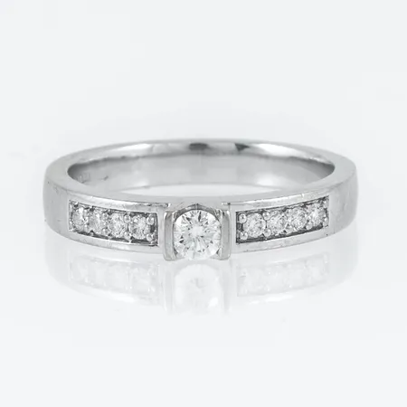 Ring i 18K vitguld med 1 x c:a 0,15ct och 8 x c:a 0,015ct briljantslipade diamanter. Den är i storlek 18½, är 3 - 3,5 mm bred och väger 5,2g. Stämplad GHA (Guldfynd), 750.