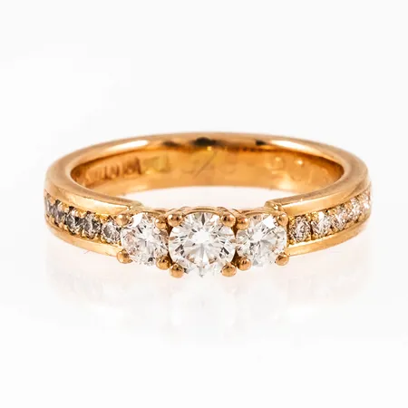 Ring i 18K guld med 1 x 0,27ct (Tw(G)/vs1), 2 x c:a 0,15ct och 12 x c:a 0,015ct briljantslipade diamanter. Den är i storlek 17, är 3,5 - 4 mm bred och väger 5,3g. Fint skick. GIA-certifikat (fr. juni 2013) för mittstenen medföljer. Stämplad JML, 18K & kattfot. Gravyr.