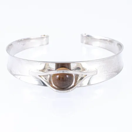 Armring i silver (925/1000) med tigeröga. Den är 5 - 14 mm bred, innermått 18,5 cm, öppning 18 mm. Vikt: 23,3g. Elis Kauppi, Kupittaan Kulta Oy, Finland.