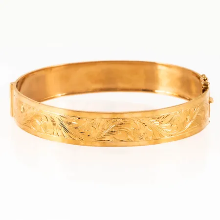 Armring i 18K guld med fint handgraverat mönster. Det är 11,5 mm brett, innermått 18 cm, 60,5 x 51,5 mm, öppningsbar, kistlås. Vikt: 12,1g. Stämplad B9 (1952), ABJ (Juvelfabriken AB, Stockholm), 18K & kattfot.