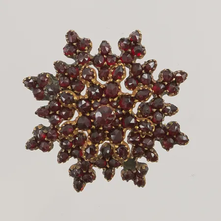 Brosch, stjärna med granater, 40x40mm, sannolikt 1900-talets första hälft, en sten saknas, böjd vid ena stjärnspetsen, oädel metall