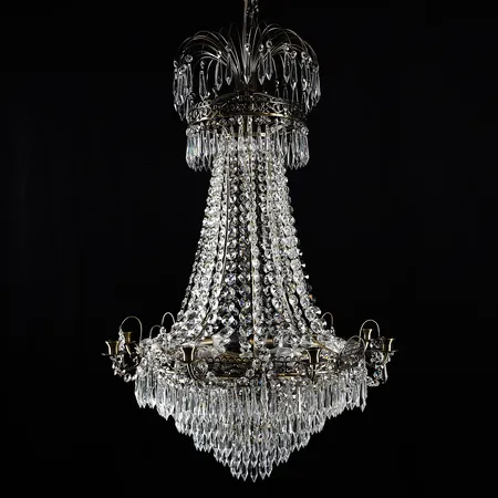 Ljuskrona för åtta ljus, Empirestil, "Läckö", Markslöjd, modern tillverkning, metallstomme, behängd med olikslipade prismor i bland annat krönande plym och avslutande piggbotten, 5 elektriska ljuspunkter, höjd ca 90cm, bredd ca 60cm, originalkartong med skador, några prismor saknas, ej funktionstestad. Specialfrakt, kontakta pantbankskontoret för mer information.