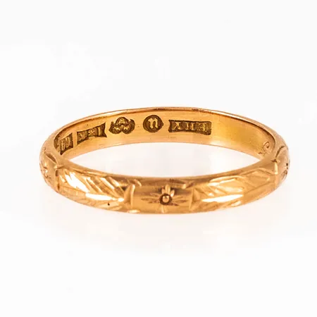 Ring i 18K guld med utvändig mönstergravyr. den är i storlek 19¼, är 3,5 mm bred och väger 3,5g. Stämplad C9 (1953), EHY (E H Yttergrens Guldsmedsaffär, Umeå), 18K, kattfot. Gravyr.