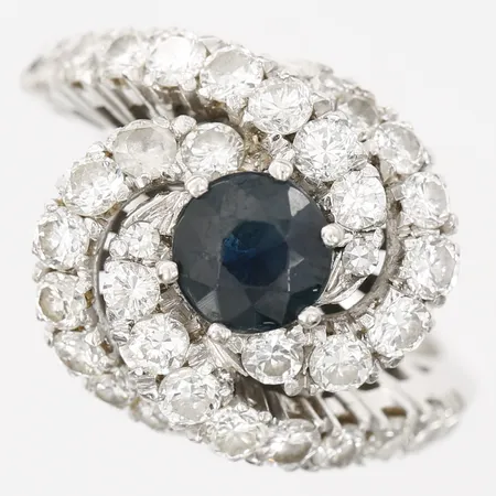 Ring med mörkblå safir ca 1,00ct samt briljantslipade diamanter 35 x ca 0,03ct, stl: 16¼, bredd: 15mm, slitage på safir, 18K vitguld Vikt: 5,9 g