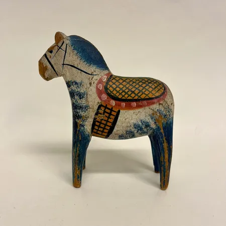 Dalahäst, tidigt 1900-tal, bemålad i blått, gult, rött och grönt mot vit botten, troligen Vattnäs, höjd 16cm, längd 13,5cm,  färg/träbortfall, slitage, sprickor. Skickas med postpaket.