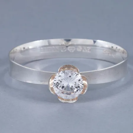 Stelt armband i silver med en vit sten (fin lyster). De är 11,3 - 6,3 mm brett och väger 21,1g.  Mittmotivet är Ø 20 mm. Fjädrande öppning. Tillverkat 1972 av Alton. Signaturstämplat KE Palmberg.