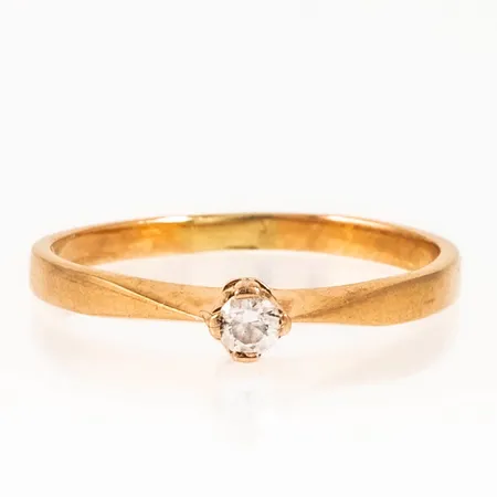 Ring i 18K guld med en vit sten (cz). Den är i storlek 17, är 1,5 - 3,5 mm bred och väger 1,8g. Något skev skena. 