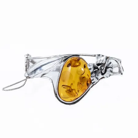 Armring i silver (835/1000) med en bärnsten c:a 31 x 22 mm. Innermått 18,5 cm, öppningsbar med säkerhetskedja. Den är 6 - 35 mm bred och väger 20,0g. Stämplad JS, 835. Dekor med vissa ojämnheter. 