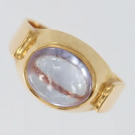 Ring med syntetisk färgväxlande safir, stl: 15¾, bredd 4-10,5mm, skev, 18K. Vikt: 5,8 g