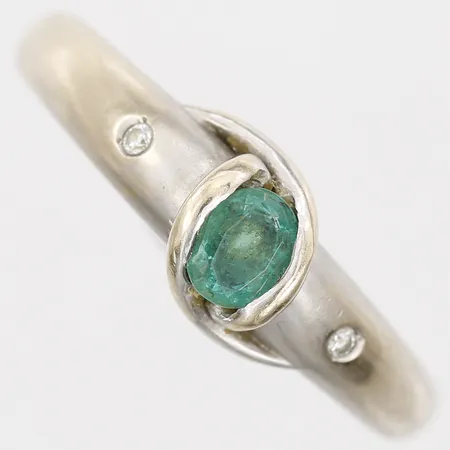 Ring med smaragd 5 x 4mm, samt briljantslipade diamanter 2 x ca 0,01ct, stl: 19½, bredd: 3 - 7mm, 18K vitguld.  Vikt: 4,3 g