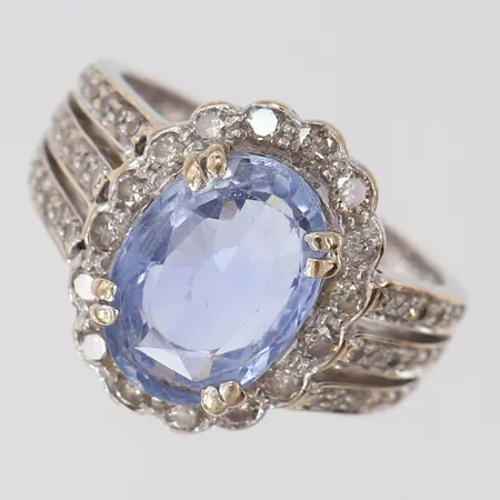 Ring med ljusblå Safir ca 4,75ct, 12,61x8,96x5,27mm, samt diamanter 42 x ca 0,01ct, 16 x ca 0,03ct, stl: 18¼, bredd 3,2-17mm, safir med nagg/slitage på fasetter, behov av omrodiering, vitguld 18K.  Vikt: 8,1 g