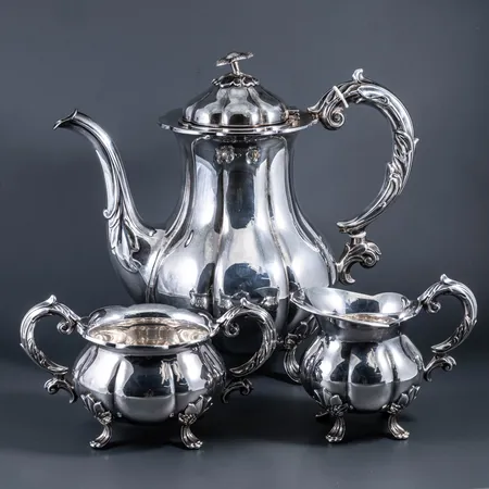 Kaffeservis i silver (830/1000): kaffekanna c:a 21,5 cm hög, gräddkanna c:a 9,5 cm hög, sockerskål c:a 8,5 cm hög. Stämplade Cohr, 830 och svenska importstämplar. De väger tillsammans 1160g. Knopp/blomma på locket kaffekannan är sned.